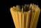 Yellow long spaghetti on black background. Thin pasta arranged in rows. Yellow italian pasta. Long spaghetti. Raw spaghetti