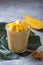 Yellow mango yogurt or smoothie on grey background. Turmeric Lassie or lassi in glass