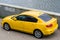 Yellow Mazda 3 car is parked on the embankment near the water. Rear side view of BK series Mazda3