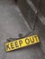 A yellow metal fluorescent keep out sign on a rusty metal chain on concrete