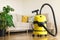 Yellow modern vacuum cleaner in living room. Copy space. Flat clean vacuuming concept. Green monstera plant