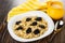 Yellow napkin, pitcher with milk, dairy oatmeal porridge with prunes in plate, spoon on wooden table