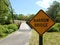 Yellow narrow bridge sign with bridge or path and trees