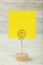 Yellow note paper on a holder on white wooden background.