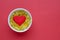 Yellow omega 3 capsules in white bowl, red heart on red background. Concept of proper nutrition, prevention of cardiovascular