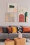 Yellow, orange, black and brown pillows on comfortable grey scandinavian sofa in bright living room interior with abstract