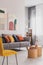 Yellow, orange, black and brown pillows on comfortable grey scandinavian sofa in bright living room interior with abstract