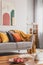 Yellow, orange, black and brown pillows on comfortable grey scandinavian sofa in bright living room interior with abstract