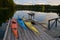 Yellow, orange, and blue kayaks on dock in evening with reflection of trees in still water