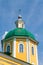 Yellow Orthodox Christian church with a green dome in summer against a blue sky with white clouds