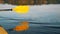 Yellow paddle reflected in lake on a kayak at sunset close-up, secluded vacation