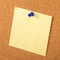 Yellow paper pined with blue tack on brown cork board background