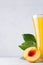 Yellow peach juice and red nectarine half with green leaves closeup soft light white wood background, vertical.