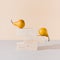 Yellow pears balancing on travertine marble blocks structure against gray and beige background.