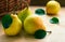 Yellow pears with green leaves laying on wooden table in front of wicker basket