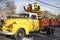 A yellow pickup truck driving in a parade with two people dressed up in costumes