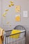 Yellow pillow in a crib, bee posters and hanging decoration in a toddler room interior. Real photo