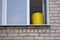 A yellow plastic bucket stands on the windowsill of an old brick house. Cleaning and washing windows