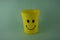 A yellow plastic cup with a smiling face, so it is very popular with children. Blue Background. Kids toys, kid friendly