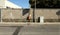 Yellow pole with small blank sign and full waste bin. Grunge concrete wall on behind, sidewalk and weathered asphalt road in front