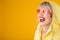 Yellow raincoat. Happy laughing woman on yellow background witn pink heart shaped sunglasses. Bright emotions