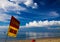 Yellow and red swim here flag against blue sky with cumulus and cirrus clouds on tropical beach in Phuket, Thailand