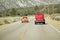 A yellow and red VW hotrod drives in opposite direction of a restored bright Red Roadster hotrod pickup truck along rural highway