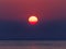 Yellow-reddish sun over ocean glowing in darkening sky by sunset