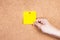 Yellow reminder sticky note on cork board with hand holding