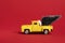 Yellow retro toy pickup carrying a Christmas tree on red background. Christmas and New Year celebration concept. Copy space,