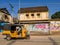 A yellow rickshaw riding past an old vintage structure with sloping roofs and