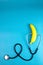 Yellow ripe banana with a stethoscope isolated on blue background