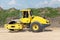 Yellow road roller for tamping soft surfaces at the construction site outside the city. Road works on an intercity highway