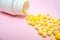 Yellow round dragees of vitamin c, ascorbic acid near a white plastic bottle, container on pink background