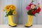 Yellow rubber boots standing on a wooden background of dirt and a flower inside