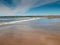 Yellow sand and blue ocean and sky. People swim in the background and surf on board. Lahinch beach in county Clare, Ireland. Warm