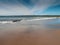 Yellow sand and blue ocean and sky. People swim in the background and surf on board. Lahinch beach in county Clare, Ireland. Warm