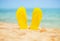 Yellow sandal flip flop on the white sand beach with blue sea and sky background in summer vacations copy space