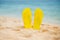 Yellow sandal flip flop on the white sand beach with blue sea and sky background in summer vacations copy space