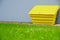 Yellow sandbox on the background of a gray basement of the house. In front of the house is a beautiful green lawn with
