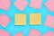 Yellow and scattered pink square blank paper stickers on blue background. Copy space