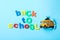 Yellow school bus and phrase `Back to school` on light blue background, flat lay