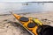 A yellow sea kayak on the sand and four kayaking along the shore