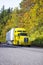 Yellow semi truck and reefer trailer driving uphill autumn road