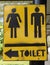 Yellow sign with male and female images and the way to the bathroom