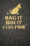 Yellow sing on a dark asphalt to dog owners to clean up dog poo. Bag it, bin it. 150 euro fine