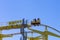 Yellow slide ride with people sitting in a small trailer against the blue sky. Extreme attraction in the amusement park