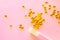 Yellow small gelatinous pills in dosage spoon for drugs and sprinkled on a pink background, close-up