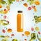 Yellow smoothie or juice bottle with flying or falling ingredients: citrus fruits, oranges and berries on light blue background