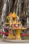 Yellow spirit house with flowers, food, incense, candle and jar
